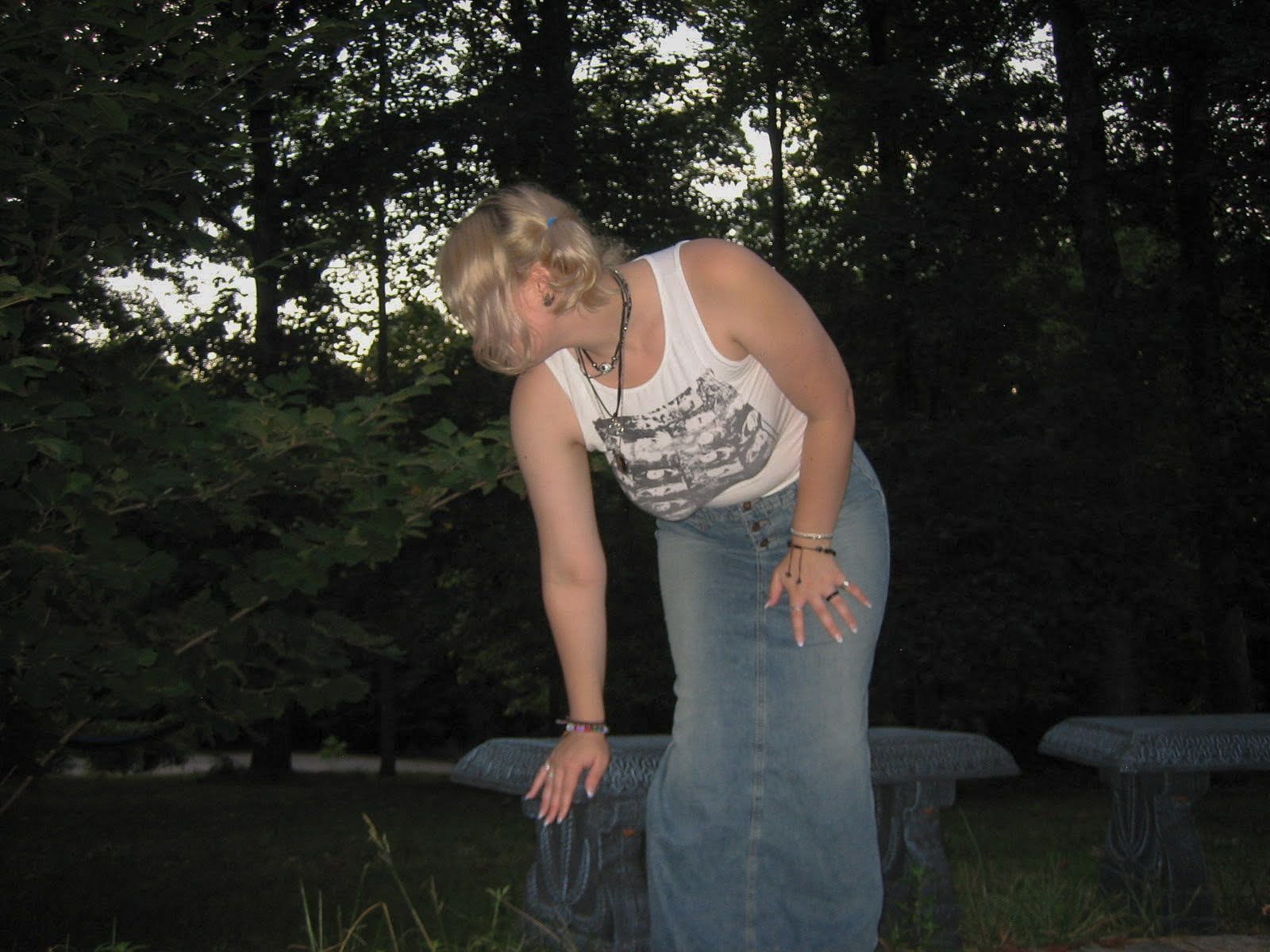 Woman leaning over to sit on a bench. 