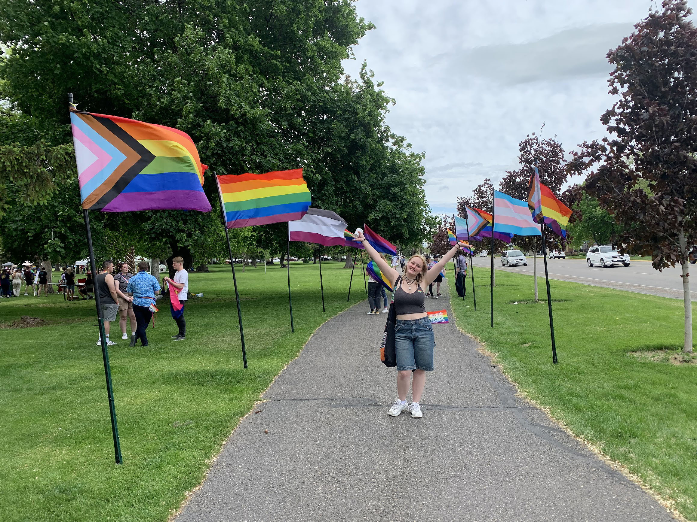 Girl standing on a sidewalk surrounded by various pride flags.