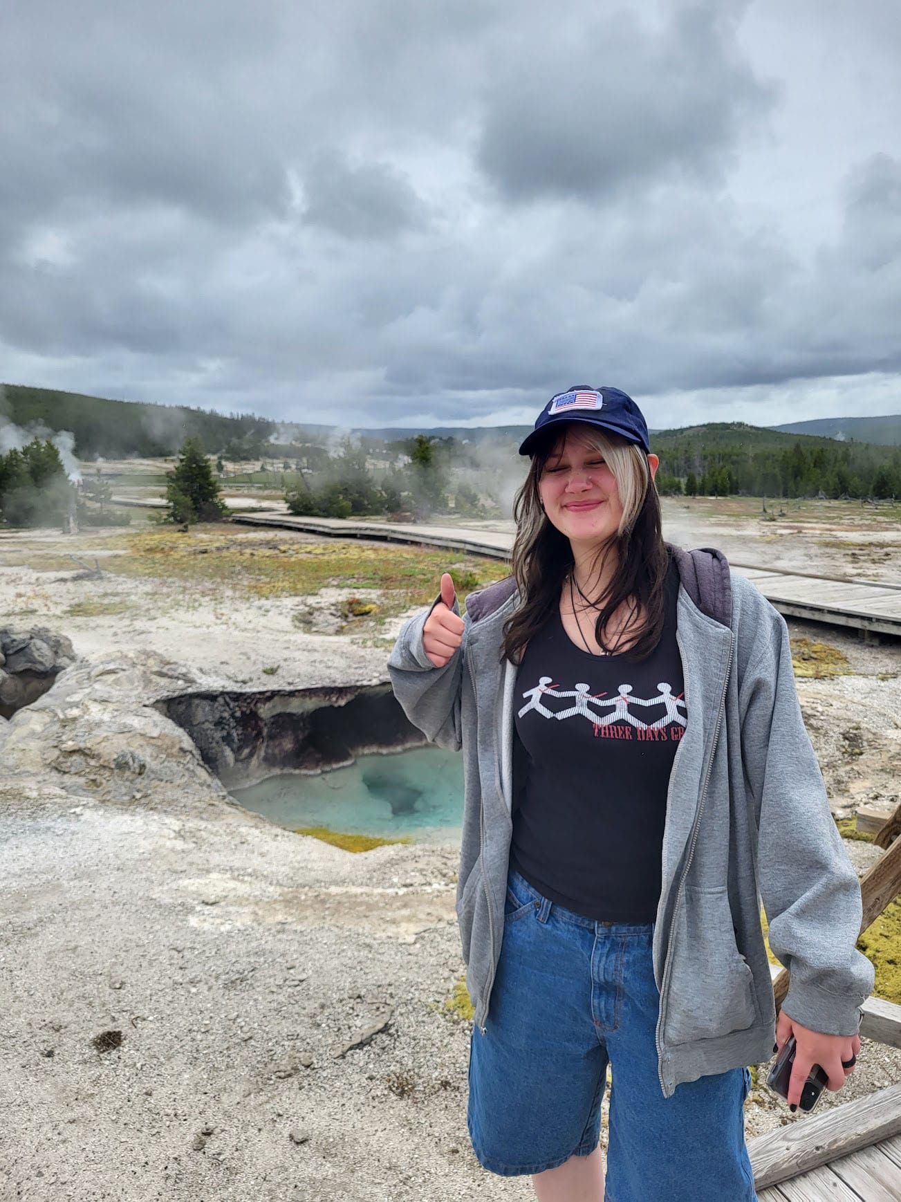 Girl standing in front of a natural geyser from Yellowstone, pointing at it. 